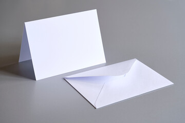 Standing blank empty rectangular greeting card and envelope mock up on grey background. For use as a Christmas, birthday, wedding or celebration background template.	
