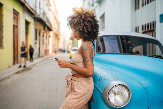 Cuban woman using smartphone near car