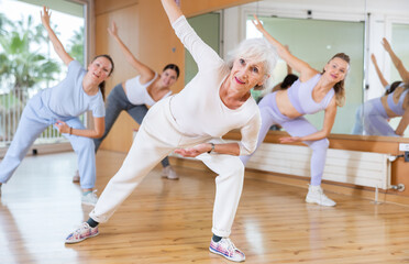 Active aged woman practicing fitness dance in training hall during dancing-classes. Women training...