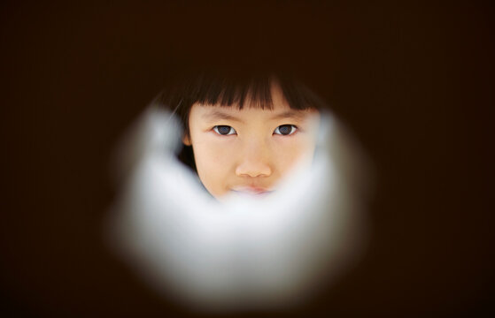 Asian girl looking at the camera through a hole in a building