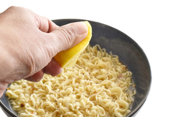 Hand squeezing lemon on instant noodle soup isolated on white background. Selective focus on the juice of lemon. 