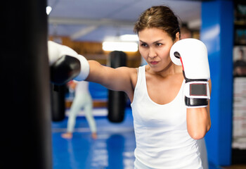 Asian woman in boxing gloves exercising jabs with punchbag during her boxing training.