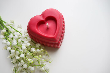 valentine's day background. candle in the shape of a heart made of natural soy wax in the shape of a heart and a bouquet of flowers