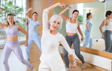 Active positive senior woman performing dance elements during lesson with female group in modern school for adults