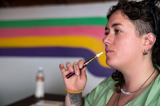 Young tattooed woman taking a drag from vape pen