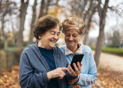 Old women in sportswear standing in park using smartphone