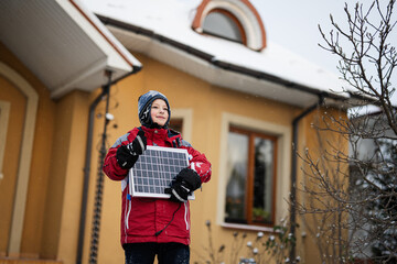 Obraz premium Boy with solar panel against house in winter. Alternative energy concept.