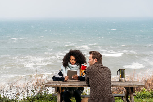 Diverse couple sitting at table against waving sea - Powered by Adobe