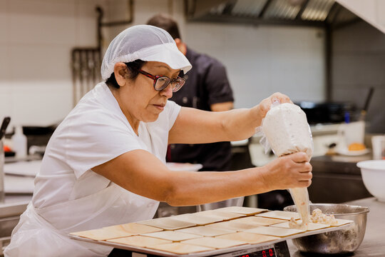 Woman baker squeezing cream on buns