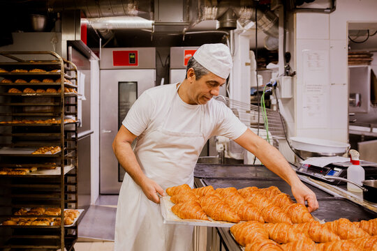 Male baker checking croissant on tray