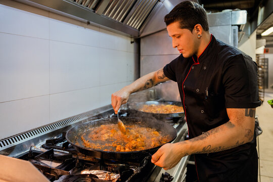Young male cook frying paella