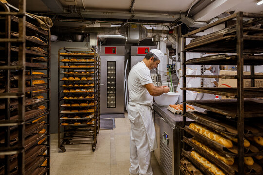 Mature baker breaking eggs for pastry