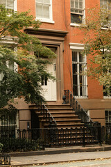 Fototapeta na wymiar brick house with white windows and entrance with stairs near autumn trees on street in New York City.