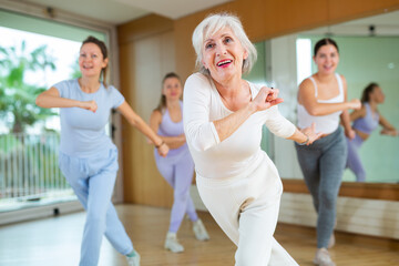 Active positive senior woman performing dance elements during lesson with female group in modern...
