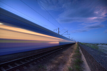 High speed train in motion on the railway station at dusk. Landscape with moving blue modern...