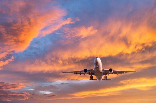 Airplane is flying in colorful sky at sunset. Landscape with passenger airplane, blue sky with orange and pink clouds. Aircraft is landing. Business and commercial. Travel. Aerial view. Transport © den-belitsky