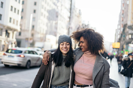Female friends walking embraced through the city in winter