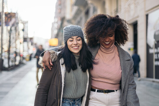 Female friends walking embraced through the city in winter