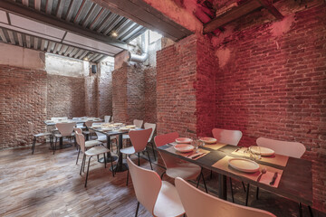 Dining room of a restaurant in a basement with rigid brick and wooden tables arranged for service and ceilings with beams and zinc-plated metal plates