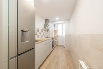 Elongated kitchen with glossy gray base units with large drawers and wooden countertop and drying terrace without doors