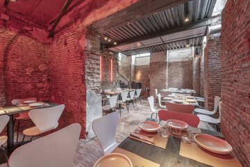 Dining room of a restaurant in a basement with the stark brick and the wooden tables arranged for the service
