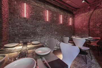 Dining room of a restaurant in a basement with rigid brick and wooden tables arranged for service and ceilings with beams and zinc-plated metal plates