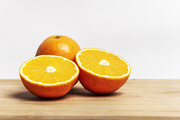 Two oranges bursting with vitamin c, one cut in half and one whole on a bamboo board with a white wall background