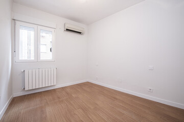 Empty room with white aluminum radiator under the window and laminate flooring