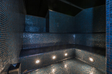 A sauna with blue glass tiles covering all surfaces