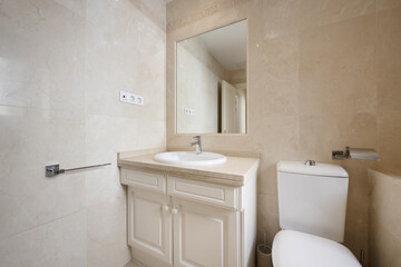 Fototapeta na wymiar Bathroom with cream-colored marble countertop on white wooden furniture, mirror integrated into the wall and tiles of the same material