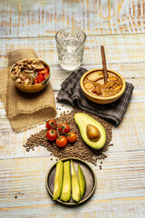 Still life with cut crystal water glass, kitchen towels, tomato and tuna salad, lentil stew and pieces of avocado and tomato on a light wooden table