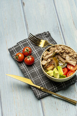 A delicious canned tuna and tomato avocado salad in a golden bowl with matching cutlery on a black cloth with some cherry tomatoes