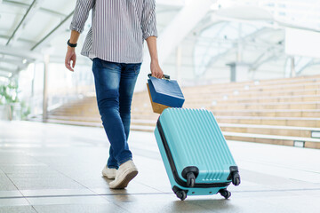Asian young man dragging a suitcase along the city or airport terminal with shopping bags.