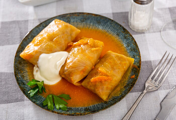 Homemade cabbage rolls in leaves of cabbage at plate with sour cream and greens