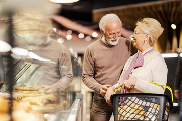A happy senior couple is buying bread and pastry at the bakery department in supermarket.
