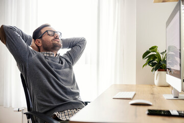 A relaxed freelancer sits in his chair and has work break at home office. - obrazy, fototapety, plakaty
