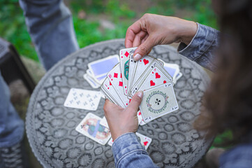 Obraz premium Card playing in a spring garden: Couple are sitting on a table, relaxing and playing cards together. Blurry background.