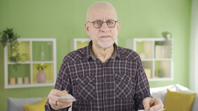 Old man getting angry at home reacting to high priced bills or receipts.
Elderly man with high spending, shopping, fuel bills holding in front of camera at home gets angry.

