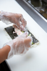 A view of hands preparing a sushi roll at an ingredient station.