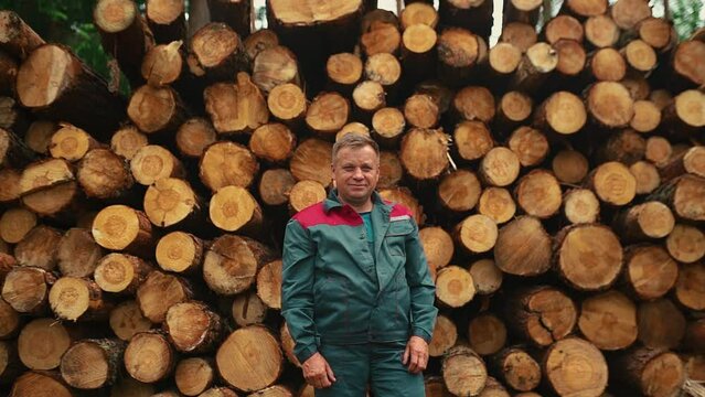 Portrait man in work clothes standing near a tree. A lumberjack against the background of stacked firewood.
