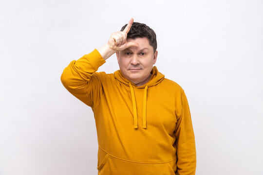 Gloomy depressed man showing looser gesture holding fingers near forehead, sad because of silly mistake, wearing urban style hoodie. Indoor studio shot isolated on white background.