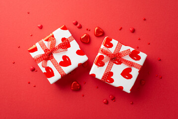 Valentine's Day concept. Top view photo of white gift boxes with ribbon bows heart shaped chocolate candies and sprinkles on isolated red background