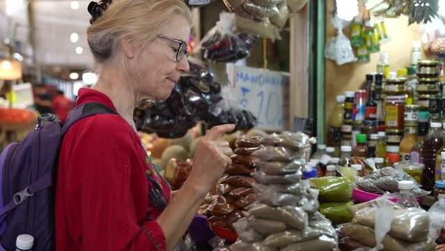 Attractive blonde mature senior woman wearing ethnic attire, buying spices at a local indoor market in Mexico.
