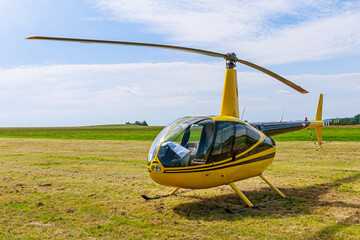 Modern light yellow helicopter on a grassy field against the blue sky. Front view.