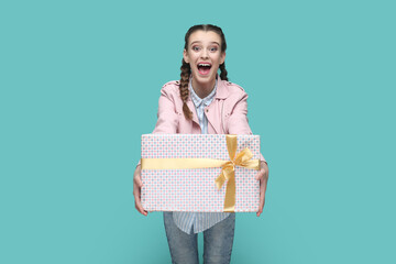Portrait of excited amazed teenager girl with braids wearing pink jacket giving wrapped present box...