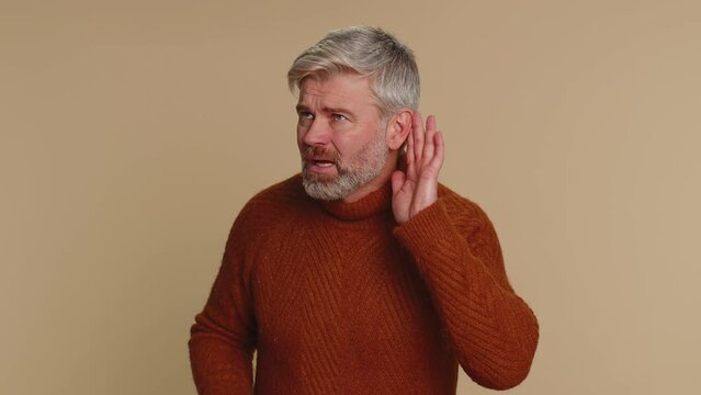 I cant hear you. What. Middle-aged old man trying hear you, looking confused and frowning, keeping arm near ear for louder voice, asking to repeat, to hear information, deafness. Senior mature guy