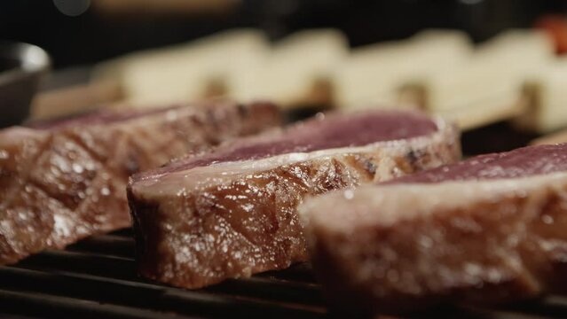 Medallions of sirloin steak being placed on the grill over the flames with coalho cheese in the background.