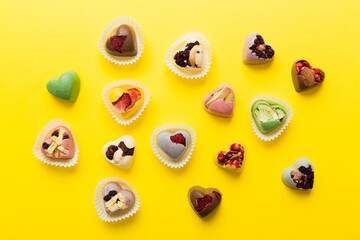 Fototapeta premium chocolate sweets in the form of a heart with fruits and nuts on a colored background. top view with space for text, holiday concept
