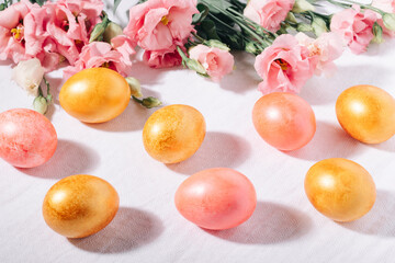 Gold and pink painted Easter eggs in pastel colors and flower bouquet on a white cotton tablecloth