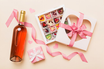 Bottle of red wine on colored background for Valentine Day with gift and chocolate. Heart shaped with gift box of chocolates top view with copy space